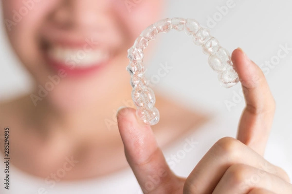 Obraz A smiling woman holding invisalign or invisible braces, orthodontic equipment