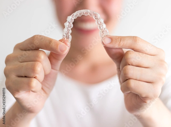 Obraz A smiling woman holding invisalign or invisible braces, orthodontic equipment