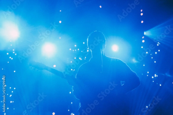 Obraz Rock band front man silhouette on a stage with guitar singing to microphone in colorful backlights 