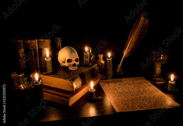 Fototapeta Wizard's Desk. A desk lit by candle light. A human skull, old books, a goblet, and potion bottles are present. Desk has parchment paper with arcane writing. Feather pen in inkwell. Focus on skull.