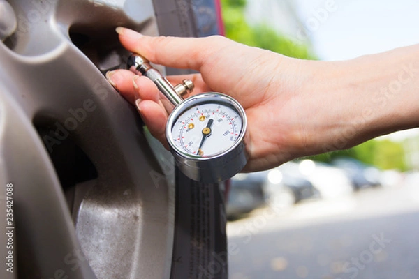 Fototapeta Checking car tyre pressure with gauge