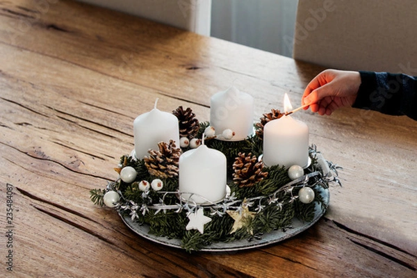 Fototapeta Close up of lighting the first candle on Advent Wreath on the first Sunday in December. Celebrating Christmas holidays, swiss tradition.
