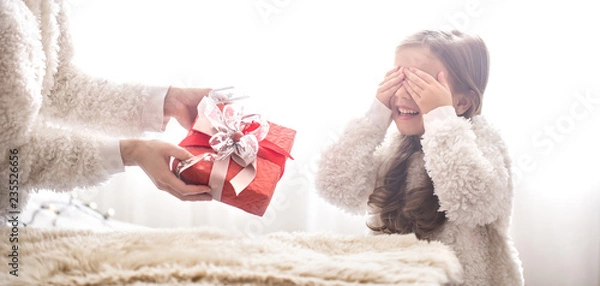 Fototapeta Christmas concept, Mom gives a gift to a little cute daughter, a place to text on a light background