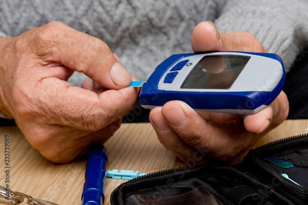 Fototapeta Concept diabetes in the elderly retired. Senior man with glucometer checking blood sugar level at home. Learn to use a glucometer