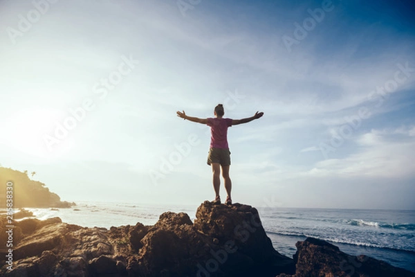 Fototapeta Freedom woman outstretched arms on sunrise seaside rock cliff edge