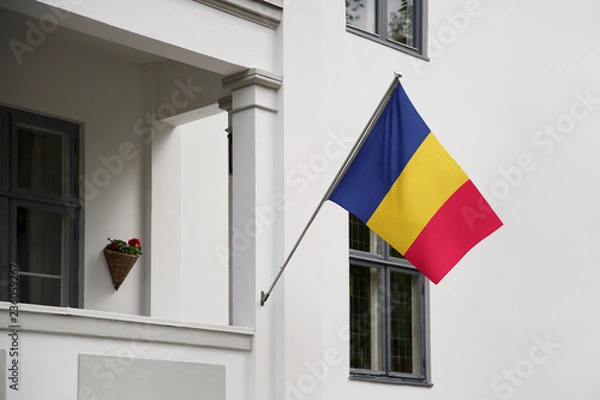 Fototapeta Chad flag hanging on a pole in front of the house. National flag waving on a home displaying on a pole on a front door of a building and raised at a full staff.