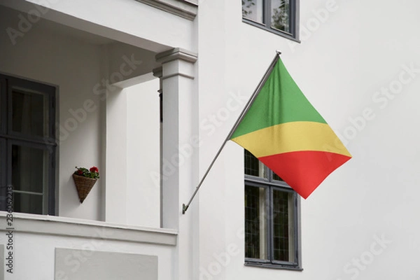 Fototapeta Congo flag hanging on a pole in front of the house. National flag waving on a home displaying on a pole on a front door of a building and raised at a full staff.