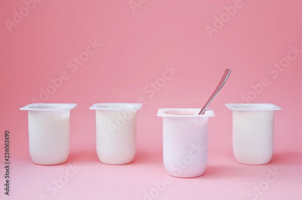 Fototapeta Four yogurts in white plastic cups on pink background with copy space. Strawberry pink yoghurt with spoon in it. Minimal style. Concept of better choice.