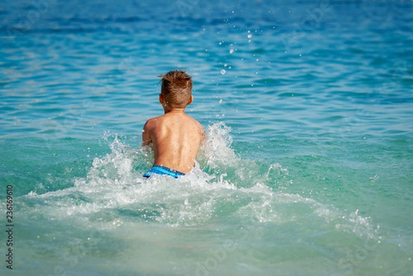 Obraz Cute European boy in a striped swimming pants spending his holidays at the sea. He is swimming in the water making a lots of splashes around.