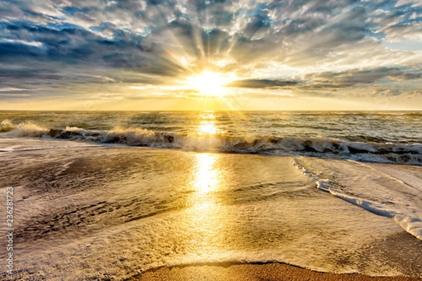 Fototapeta scenic sunset over stormy sea beach with setting sun rays coming through dramatic clouds on orange blue sky reflecting on water panoramic aerial nature dusk atmosphere evening landscape background