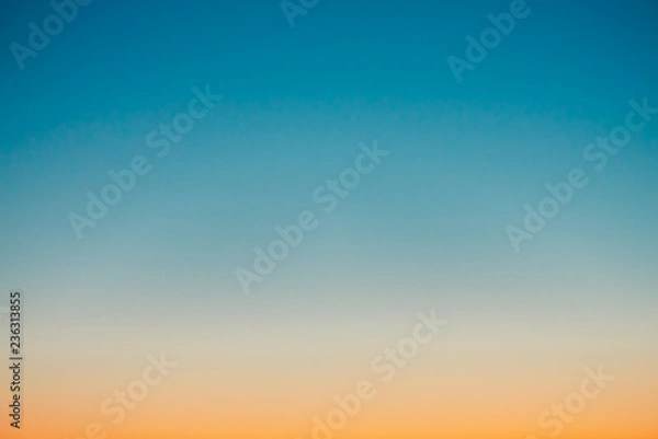Fototapeta Predawn clear sky with orange horizon and blue atmosphere. Smooth orange blue gradient of dawn sky. Background of beginning of day. Heaven at early morning with copy space. Sunset, sunrise backdrop.