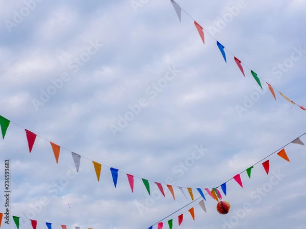 Fototapeta Row of colorful triangles flags on blue sky with clouds background in carnival fair