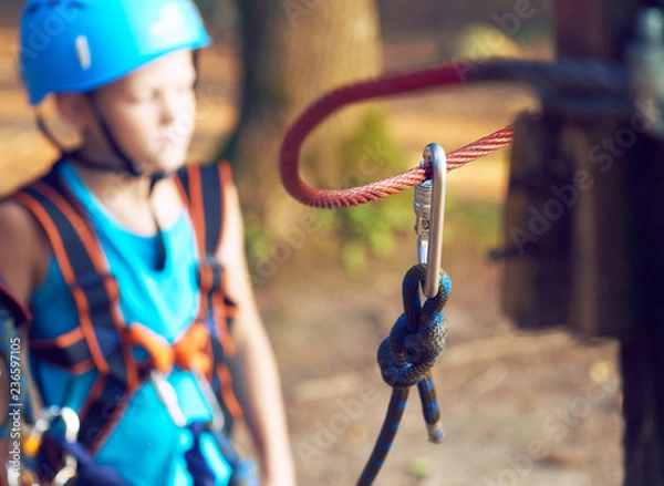 Fototapeta Cute little boy in blue shirt and helmet having fun at the adventure park, holding ropes and prepering to climb wooden stairs. Hobby, active lifestyle concept.