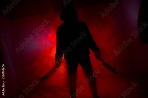 Fototapeta A dangerous hooded man standing in the dark and holding a knife. Face can not be seen. Committing a crime concept. Selective focus