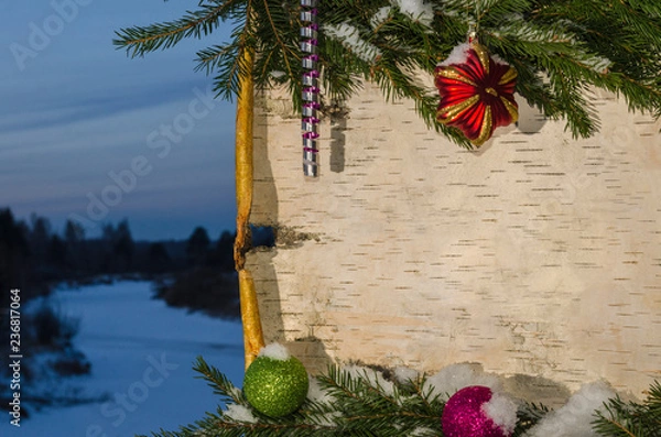 Obraz Новогодняя композиция в виде поздравительной открытки из березовой коры украшенной еловыми ветками и новогодними игрушками на фоне зимнего пейзажа.