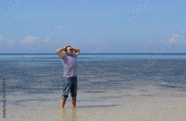 Fototapeta A man stands in the sea in the Philippines and with his hands behind his head looking thoughtfully into the distance