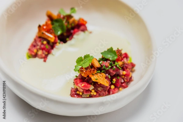Fototapeta Meat tartare with mushrooms, sauce and greenery on a white plate