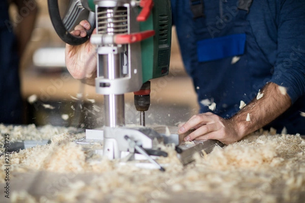 Obraz Close up of unrecognizable worker drilling wood, focus on woodchips flying from under boring mill, copy space