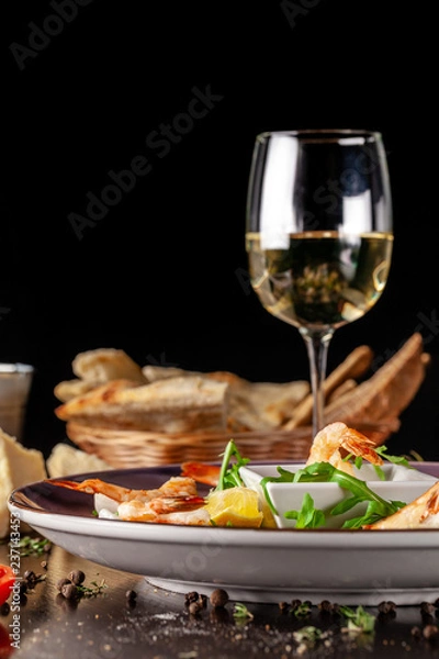 Fototapeta The concept of Italian cuisine. Tiger prawns on rice chips in a creamy sauce. Arugula salad and lemon. On the table is a glass of red wine. beautiful serving in the restaurant