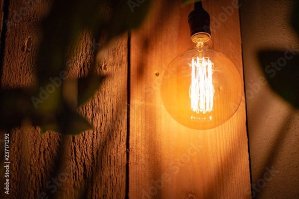 Fototapeta Design lamp with old-fashioned filament hanging in front of a scaffold wood wall