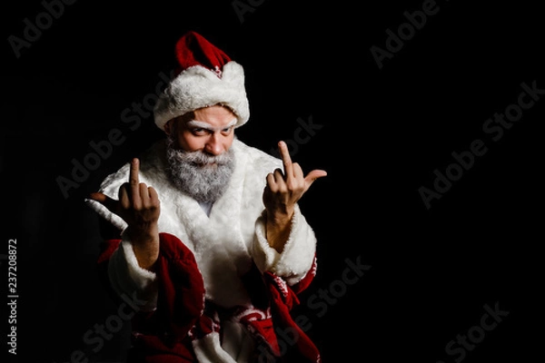 Fototapeta Portrait of a bad brutal mature Santa Claus showing middle finger signs, isolated on black background