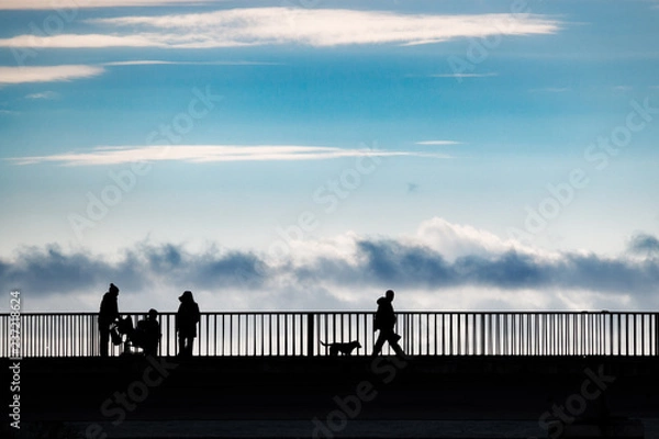 Obraz People in silhouette standing on a bridge over a sea