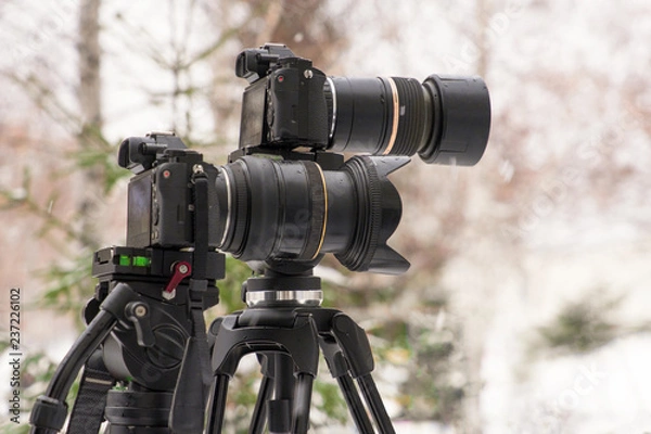Fototapeta Two cameras on a tripod shoot a report about the weather during a snowfall.