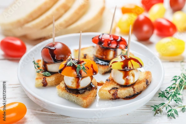 Fototapeta Tosty z chleba z pomidorami cherry, mozzarellą, tymiankiem i polewą balsamiczną na białym tle drewnianych. Canape. bruschetta. Wyśmienita przekąska. Selektywna ostrość