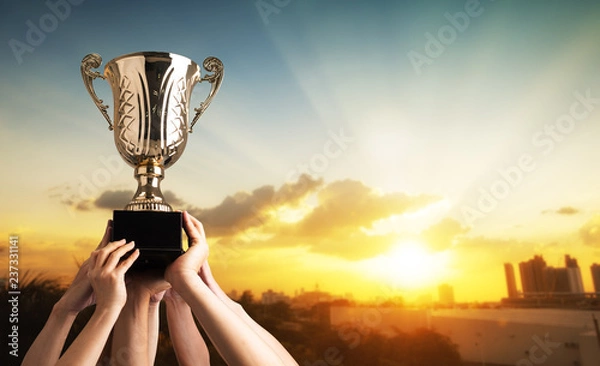 Fototapeta Winning team raise trophy cup with background of sky of light ray