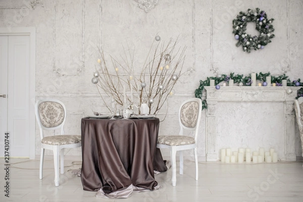 Fototapeta A winter studio background: a table with two chairs near a white fireplace and a door