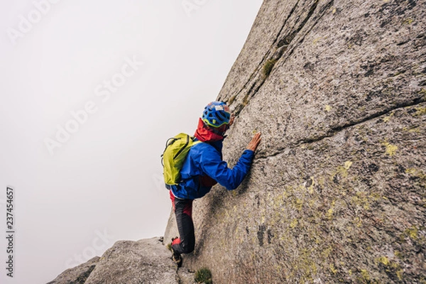 Fototapeta A solo climber ascending a steep rock face. Dangerous climb in a big wall without rope or protection. Free solo.