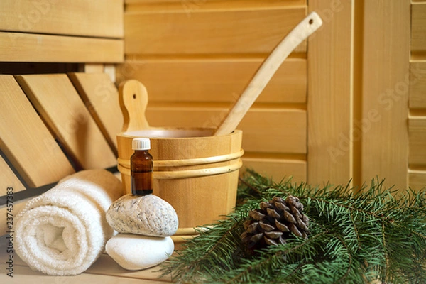 Fototapeta Spa, sauna and wellness setting with water bucket, oil essence, cones, Christmas tree branches, white towel on wooden background. winter wellness concept relax and treatment therapy. Selective focus