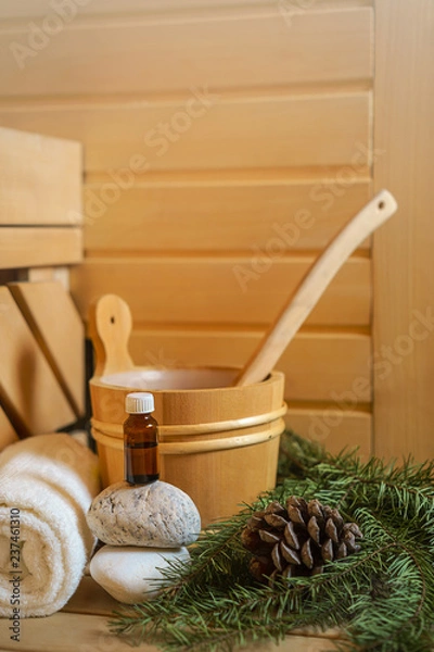 Fototapeta Spa, sauna and wellness setting with water bucket, oil essence, cones, Christmas tree branches, white towel on wooden background. winter wellness concept relax and treatment therapy. Selective focus