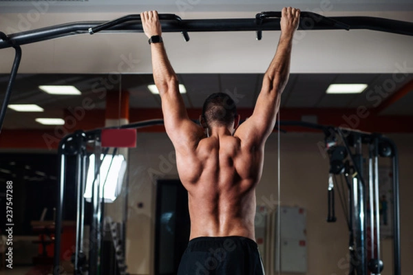 Fototapeta Athletic man making pull-up exercises on a crossbar in the gym