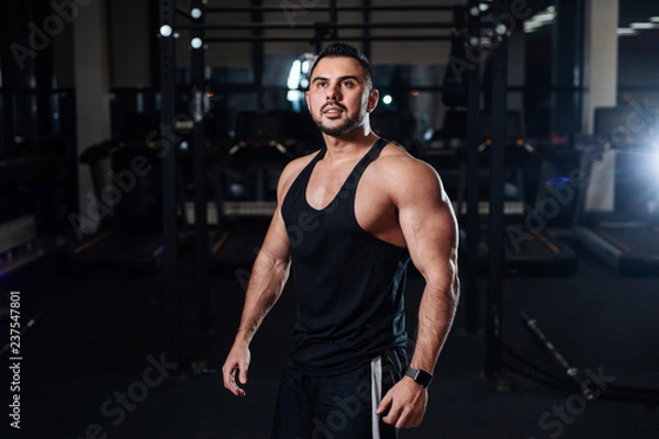 Fototapeta Athletic man posing, showing off his muscles in the gym