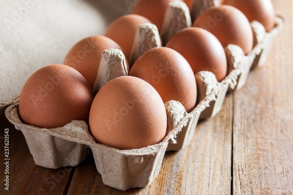 Fototapeta Large brown chicken eggs in green carton box on wooden table.
