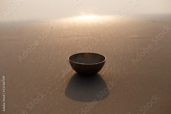 Obraz Tibetan singing bowl on the ocean on the sand. The background is blurred by sunlight. Place for inscription. Photo for advertising.