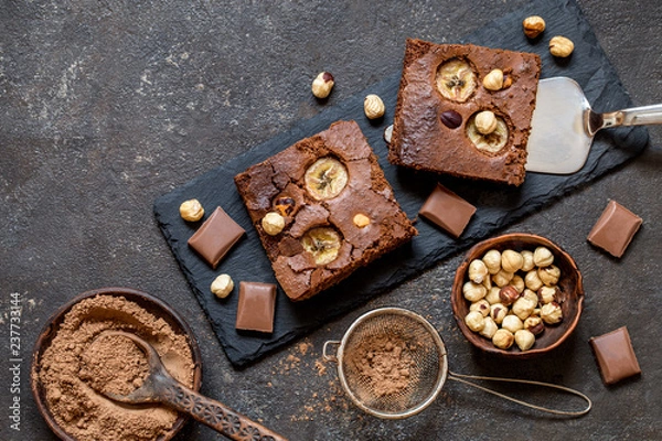 Fototapeta brownie with banana and hazelnut on black slate plates on dark background