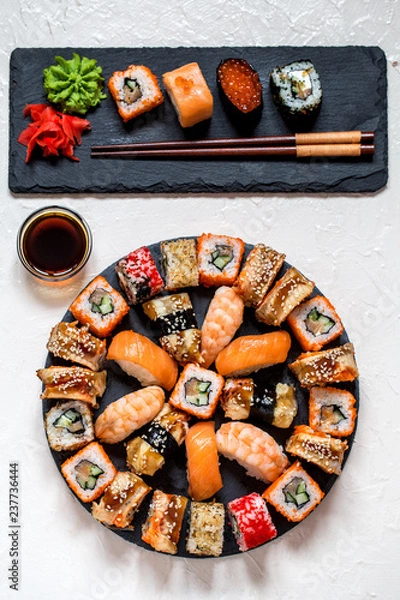 Fototapeta sushi rolls Asian food on round slate black Board with wasabi and ginger, soy sauce on white background with black slate rectangular plate