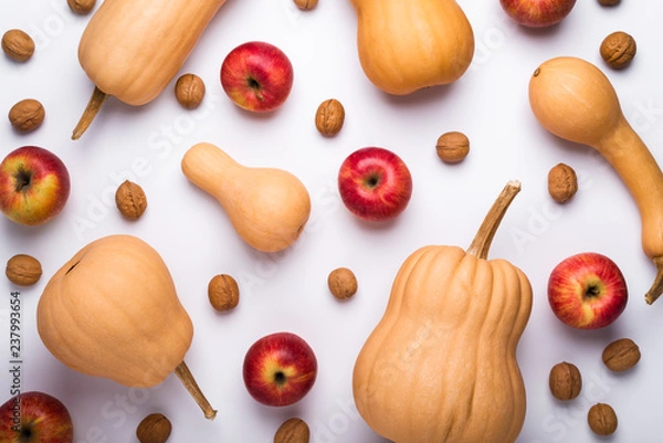 Fototapeta Pumpkins, apples, and walnuts scattered on white background, top view