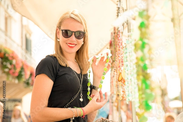 Obraz joung beautiful blond woman on the market are looking for some gifs, sunglasses and bags. she is shopping on a sunny day in italy on her travel
