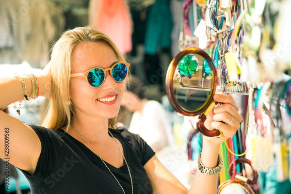 Obraz joung beautiful blond woman on the market are looking for some gifs, sunglasses and bags. she is shopping on a sunny day in italy on her travel