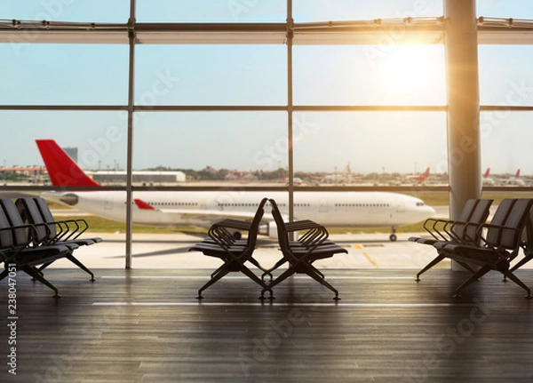 Obraz Interior inside the airport terminal with chairs in waiting departure area and view of airplane passing outside.