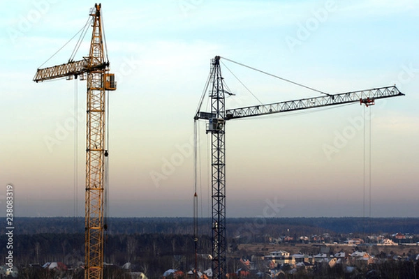 Fototapeta Two high cranes on the construction site in on sunset. Background building