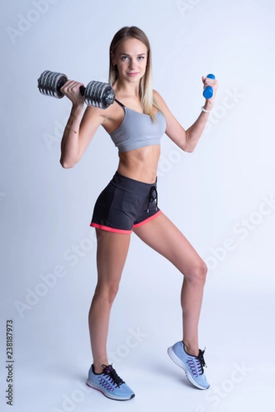 Fototapeta Beautiful young slim girl with dumbbells on a white background. Novice athlete