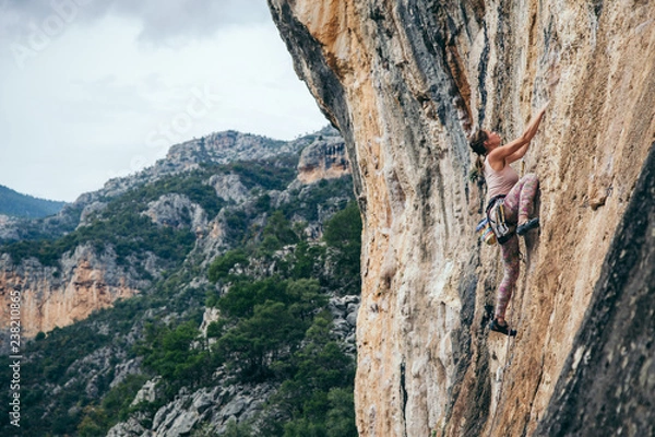 Fototapeta woman climbs a rock in Greece and beautiful forest and cliff landscape on the background