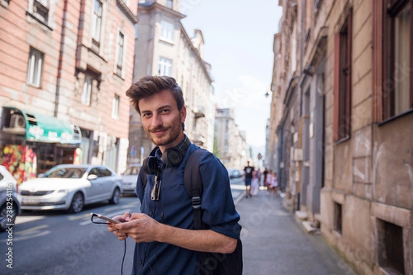Fototapeta Portrait of cheerful young tourist using phone on the street