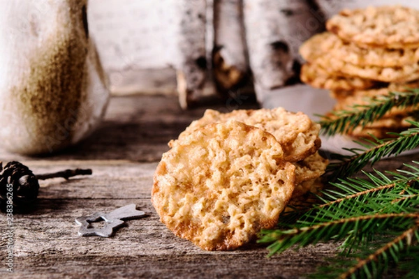 Fototapeta Havreflarn - scandinavian crispy slim oatmeal cookies, fir and birch branches and bark on old wooden background. Fast and easy scandinavian pastry. Cozy winter treat. Hygge. Fika. Christmas