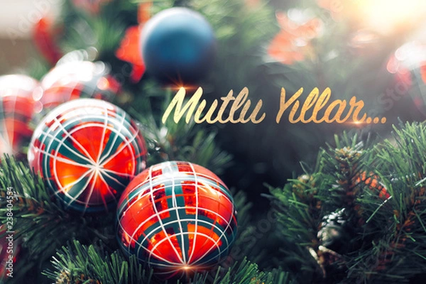 Fototapeta Closeup of shiny red bauble hanging from a decorated Christmas tree. Mutlu Yillar means Happy new year
