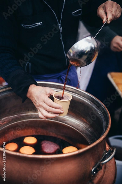 Fototapeta Pouring hot mulled wine, called Glühwein in German language, into a paper cup with a huge kitchen spoon. Favourite hot beverage at Christmas markets in Switzerland and in german-speaking countries. Ke